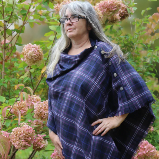 Person wearing a Scottish Heather Tartan cape in a garden setting with pink flowers.