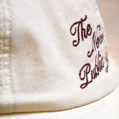 Close-up of a cream-colored cotton corduroy cap with dark burgundy embroidered script.