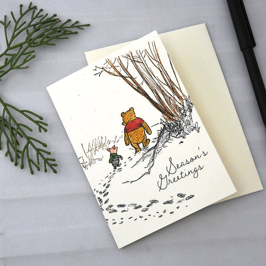 Greeting cards featuring a Winnie the Pooh and Piglet illustration walking in the forest with off-white envelopes. Text on card reads: Season's greetings.