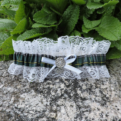 Lace garter with tartan ribbon and silver buckle on a stone surface with green leaves in the background
